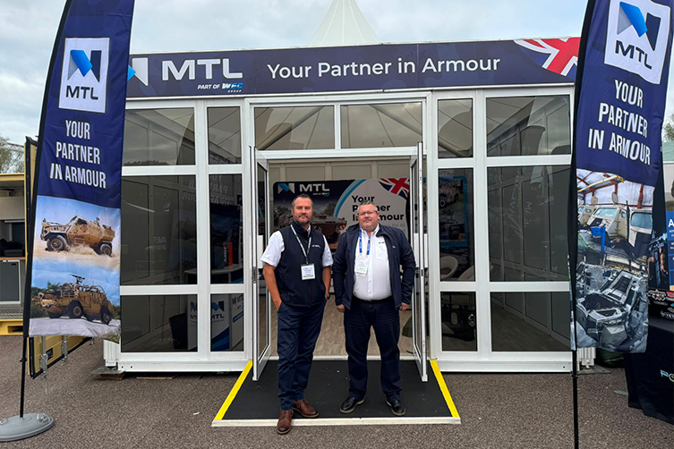 two men stood next to an MTL tradeshow stand at DVD Tradeshow stood between two flags